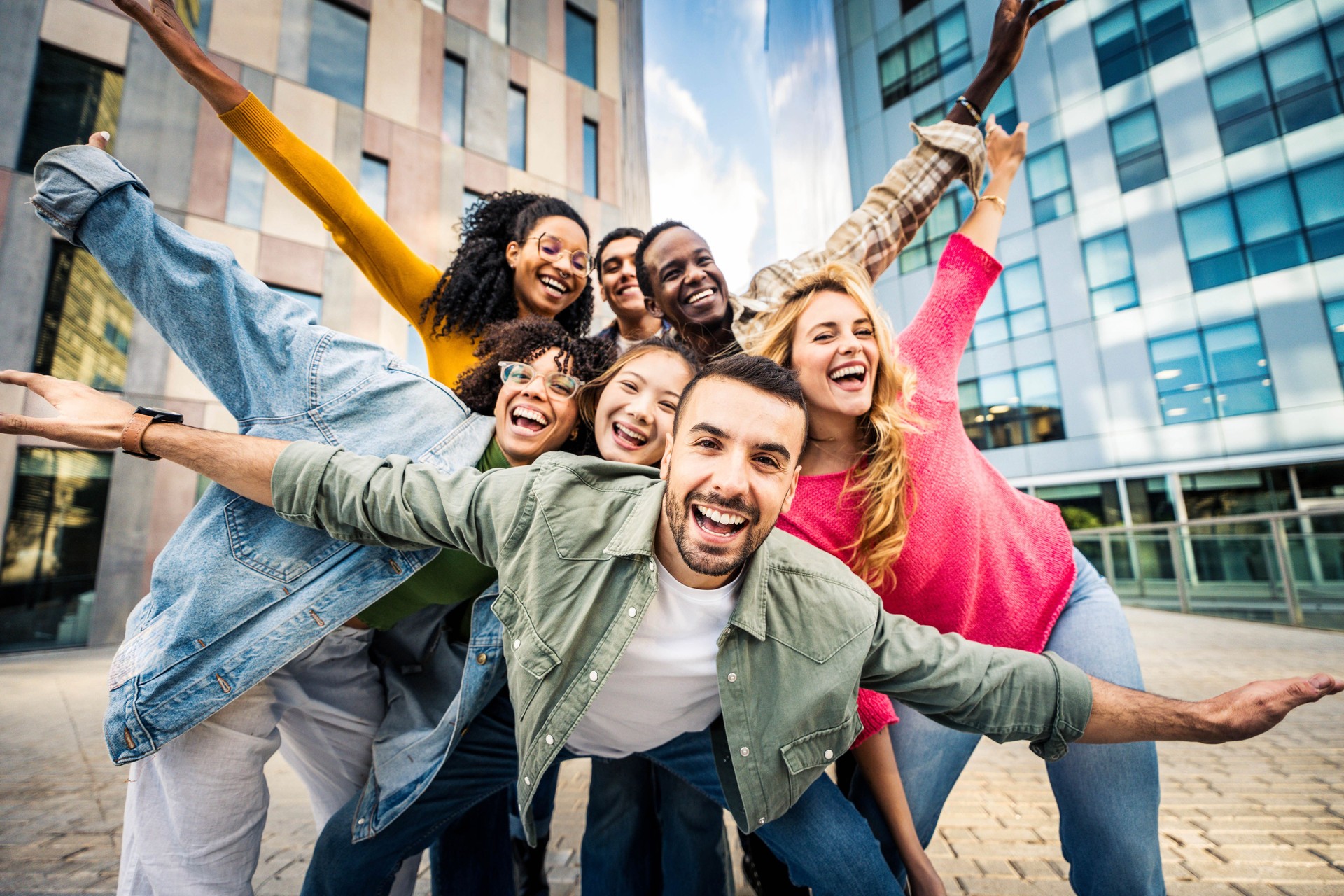 Multi ethnic young people smiling together at camera outdoors - Happy group of friends having fun hanging out in downtown street - University students standing together in college campus